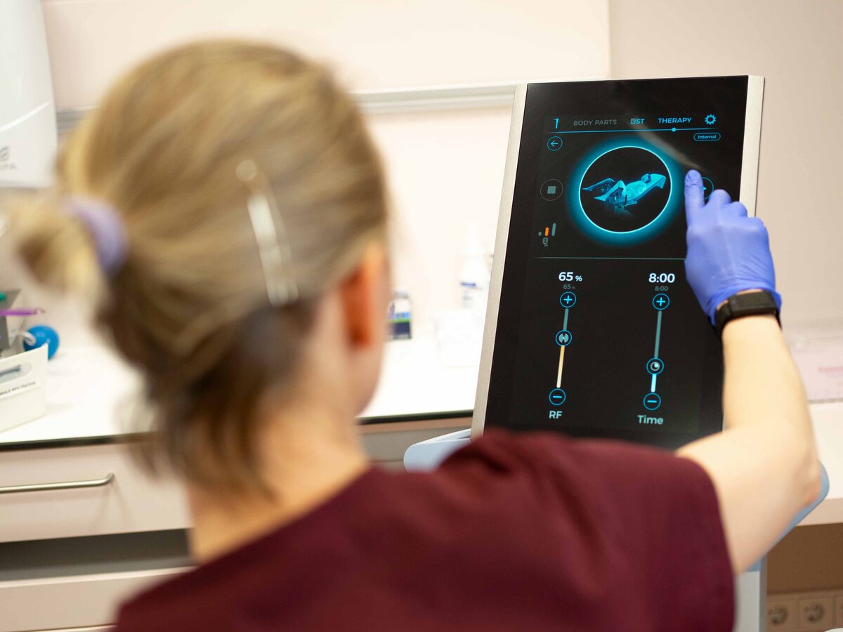 Eine Ärztin in Handschuhen stellt am Touchscreen des EMFEMME-360-Geräts Leistung und Behandlungsdauer ein.