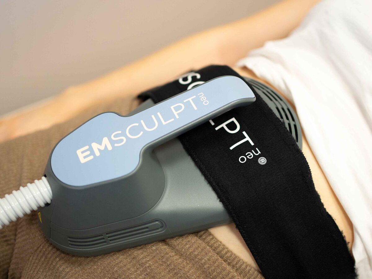 Der EMSCULPT-NEO-Applikator liegt, mit einem Gurt fixiert, auf dem Bauch einer liegenden Patientin.