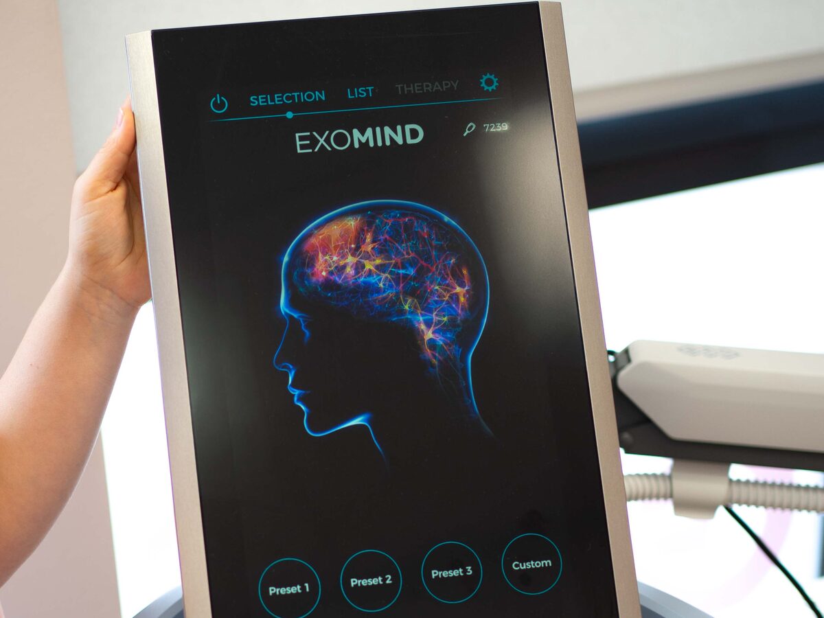 Der Bildschirm des EXOMIND-Geräts zeigt die Darstellung eines Kopfes mit leuchtenden neuronalen Netzwerken.